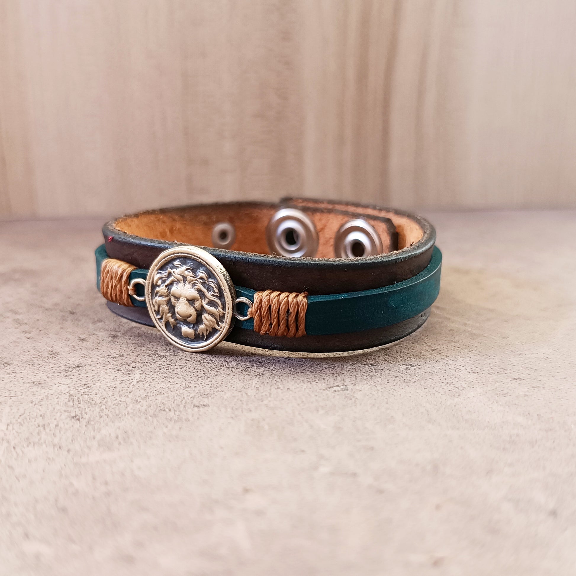 Side view of Lion's Quiet Roar Bracelet, showing layered dark brown and petrol blue Crazy Horse leather bands and detailed bronze gold cord wrap.