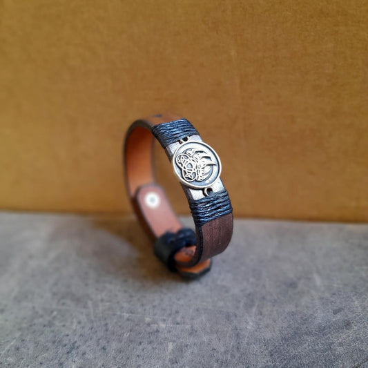 The Bear's Resolve Cuff, a dark brown hand-dyed Crazy Horse leather bracelet. Features "Let it Rip" engraved in a scratchy font, the iconic "Love you, dude" line and the Tribal Bear claw oxidized brass pendant variation with black waxed cord. Shows the unique stud button closure and blackened edges.