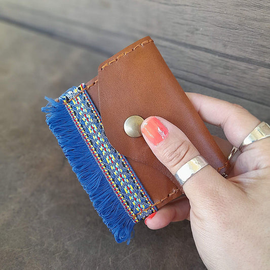 Brown leather wallet with colorful fringe held by a hand on a wooden surface