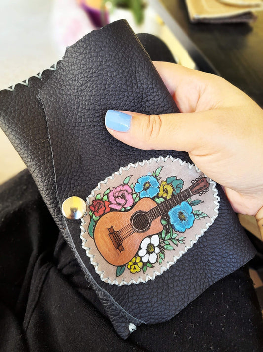The Guitar Art Pouch held in a hand, demonstrating its compact size, soft feel, and unique artistic detail.