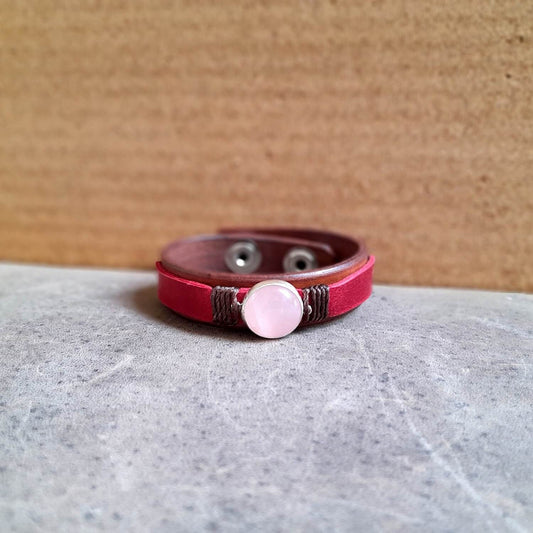 close up front view of The OOAK Red Leather Bracelet with Natural Rose Quartz: A layered brown and raspberry red full-grain leather bracelet featuring a natural rose quartz stone on a sterling silver pendant.