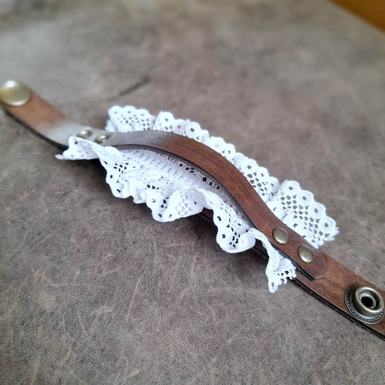 The Prairie Lace Cuff, a hand-dyed dark brown Crazy Horse leather bracelet. Features delicate lace peeking out, adorned with antique bronze stud rivets, and visible snap button closure.