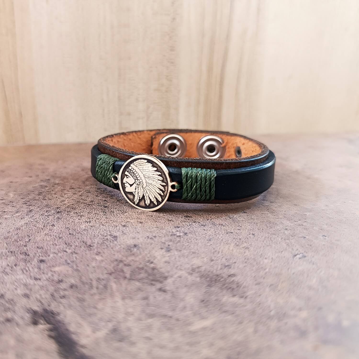 Leather bracelet with green accents and Indian Chief pendant on a textured surface.