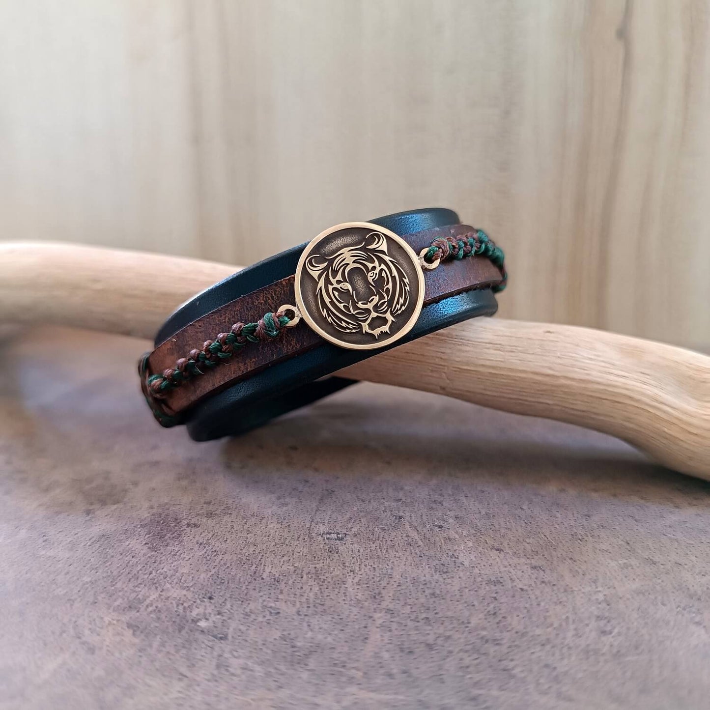 Brown and black leather bracelet with a gold tiger emblem on a wooden surface