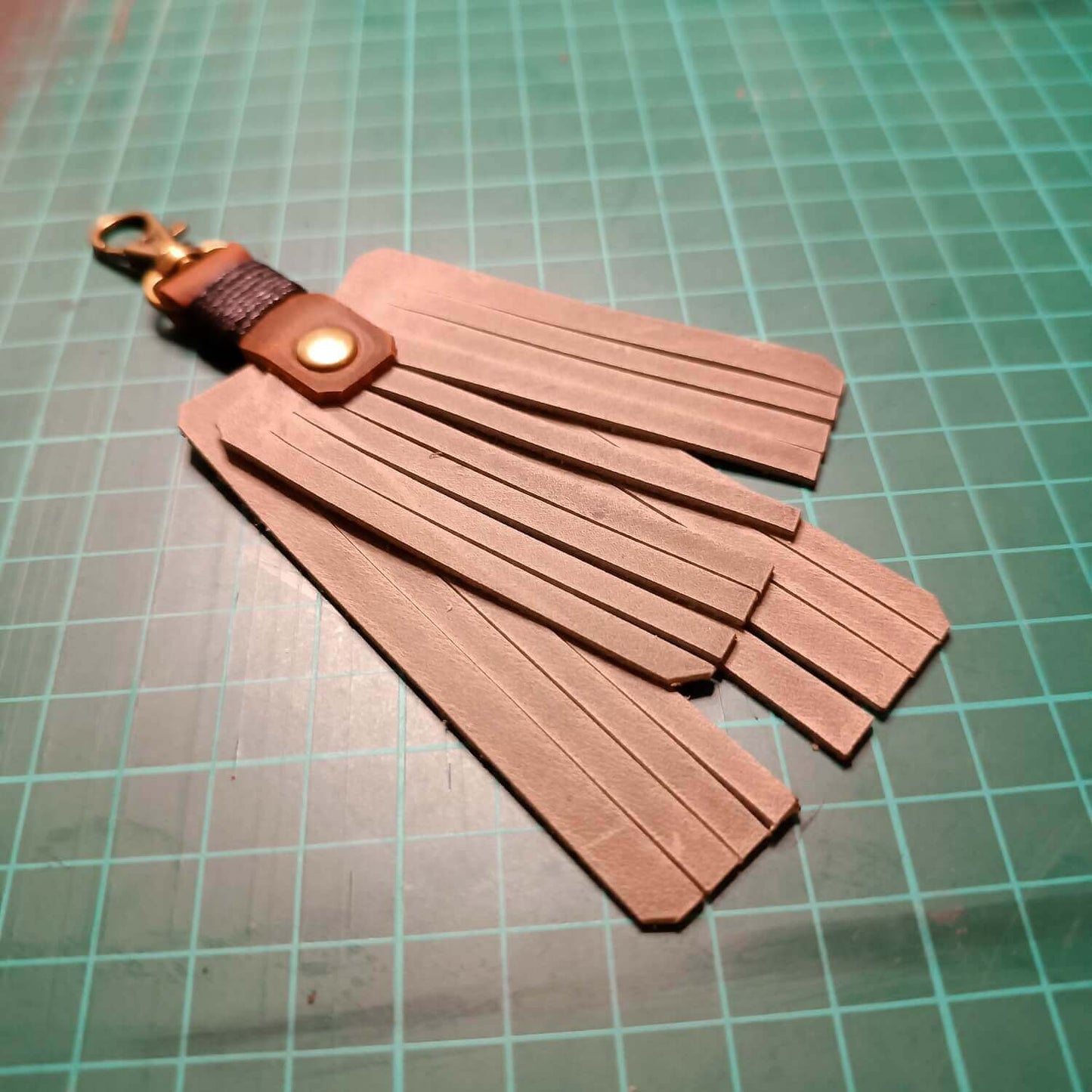 Gray leather keychain with fringes on a green grid background