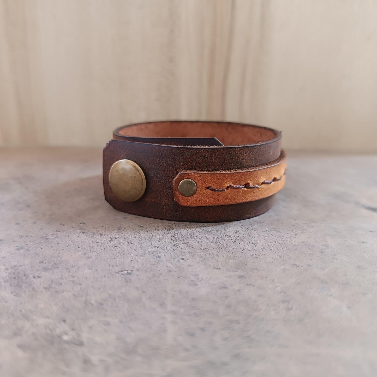 Brown leather bracelet with a gold button on a gray surface