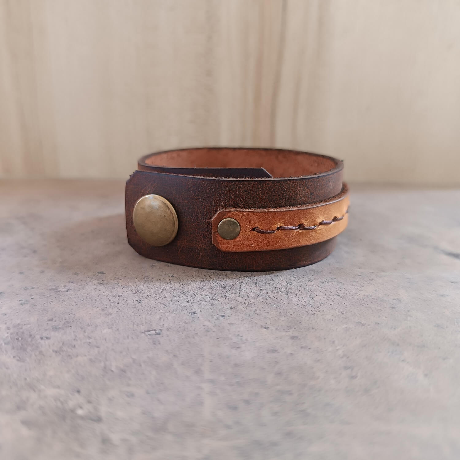 Brown leather bracelet with a gold button on a gray surface