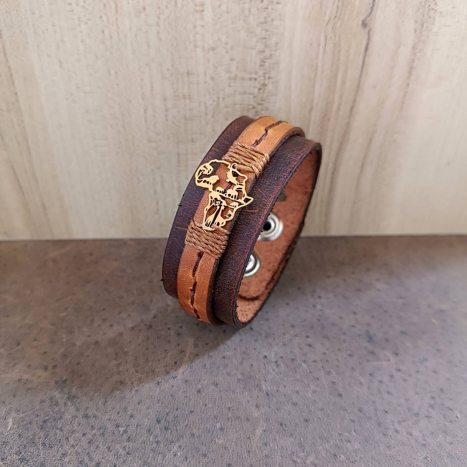 Brown leather bracelet with gold Africa Shaped pendant on a wooden surface