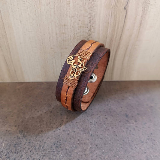 Brown leather bracelet with gold Africa Shaped pendant on a wooden surface