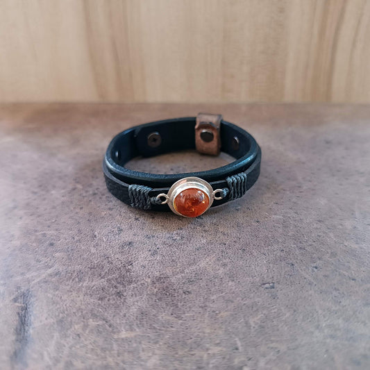 Black leather bracelet with amber stone and silver accents on a gray surface.