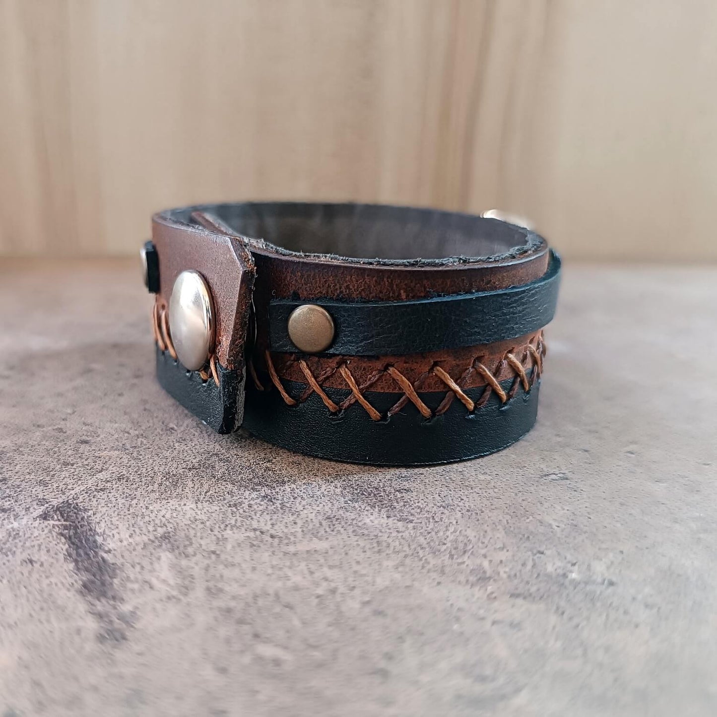 Close-up of the black and brown Crazy Horse leather layers joined by intricate 'X' pattern hand-stitching in two brown tones.