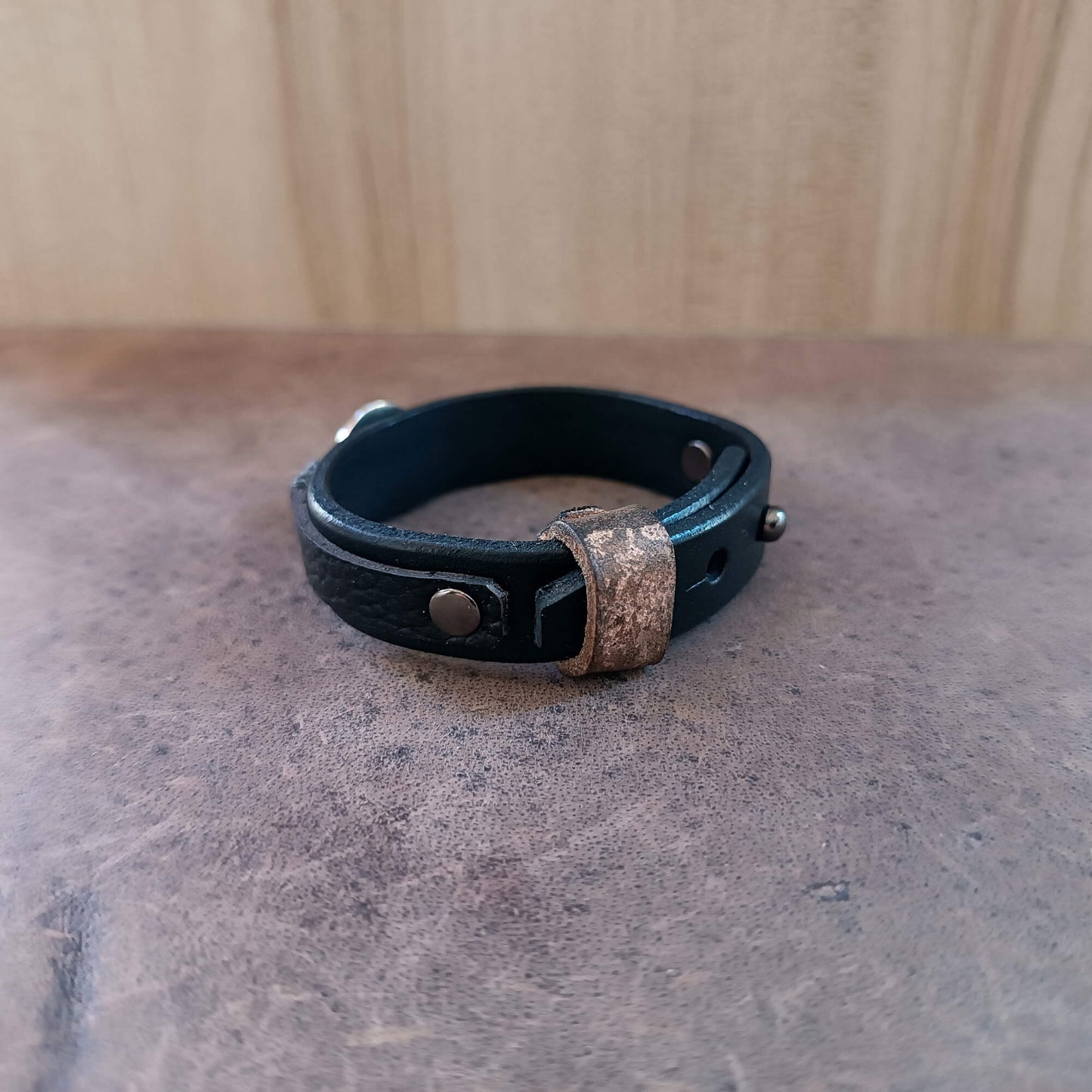 Black leather bracelet with metal clasp on a textured surface