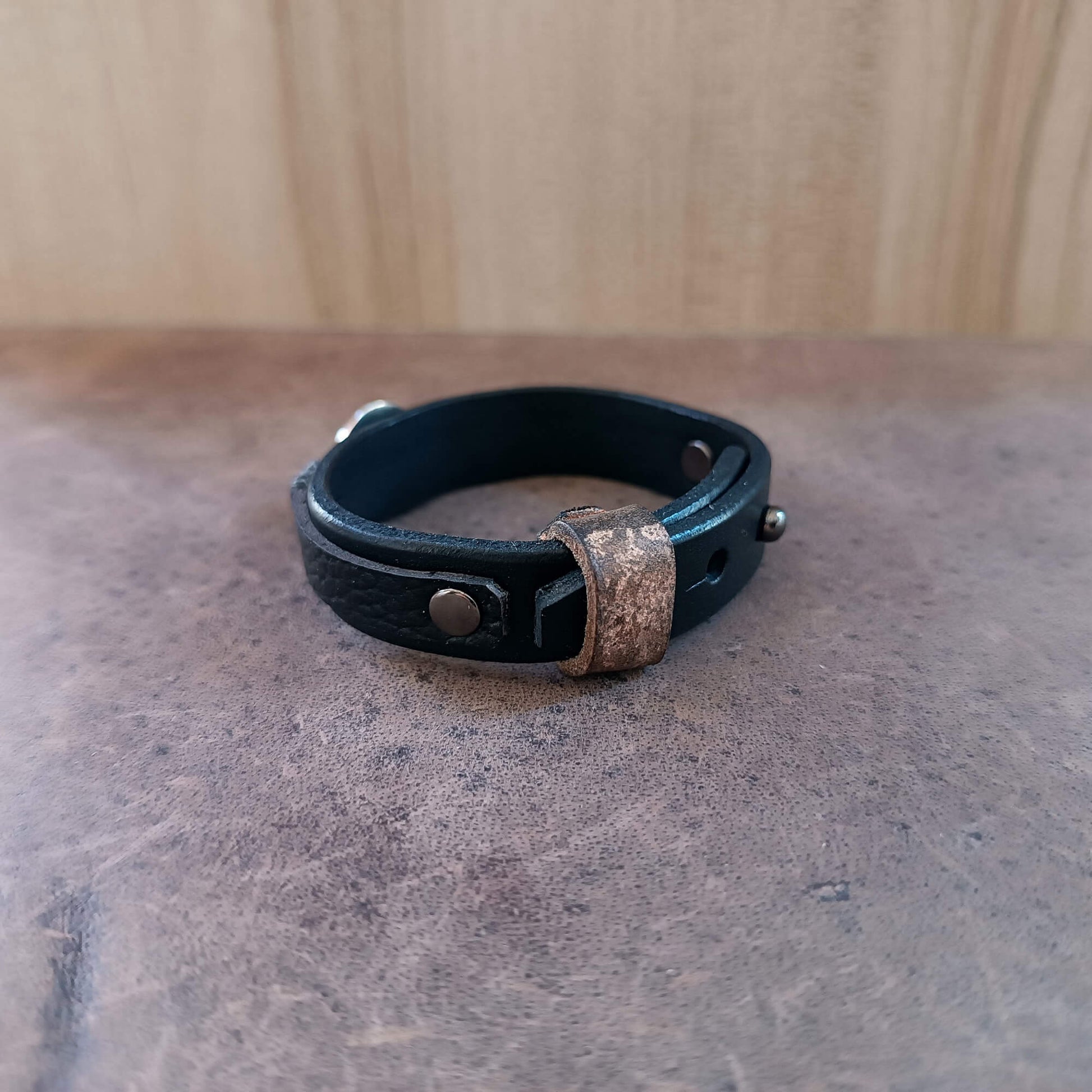 Black leather bracelet with metal clasp on a textured surface