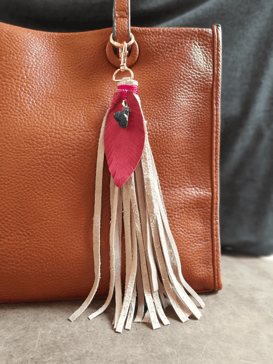 Brown leather handbag with a tassel keychain featuring a pink feather and beige fringe.