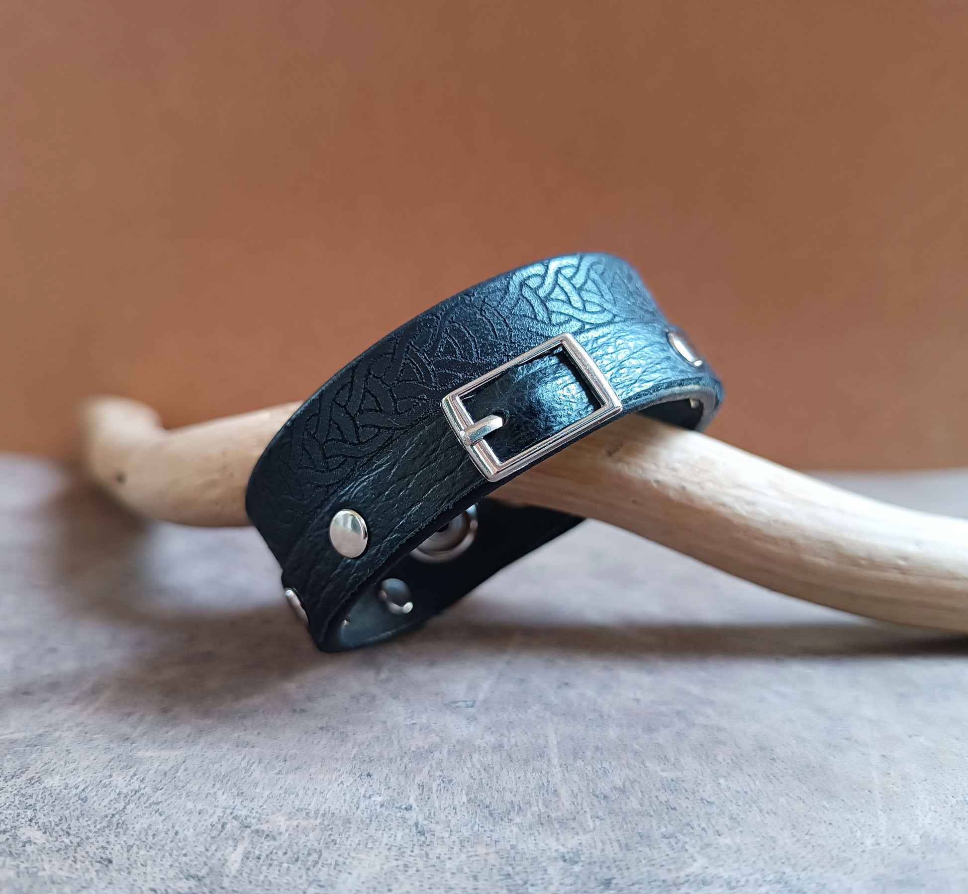 Black leather bracelet with silver buckle on a wooden stick against a brown background