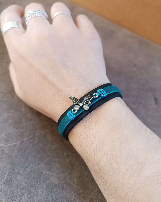 Hand wearing a blue and black bracelet with a butterfly charm on a neutral background