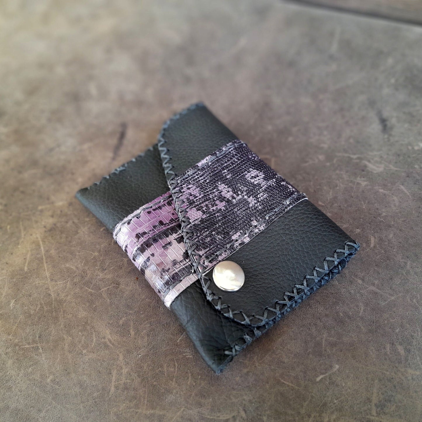 A black leather mini wallet with a purple snake print stripe, displayed on a textured surface.