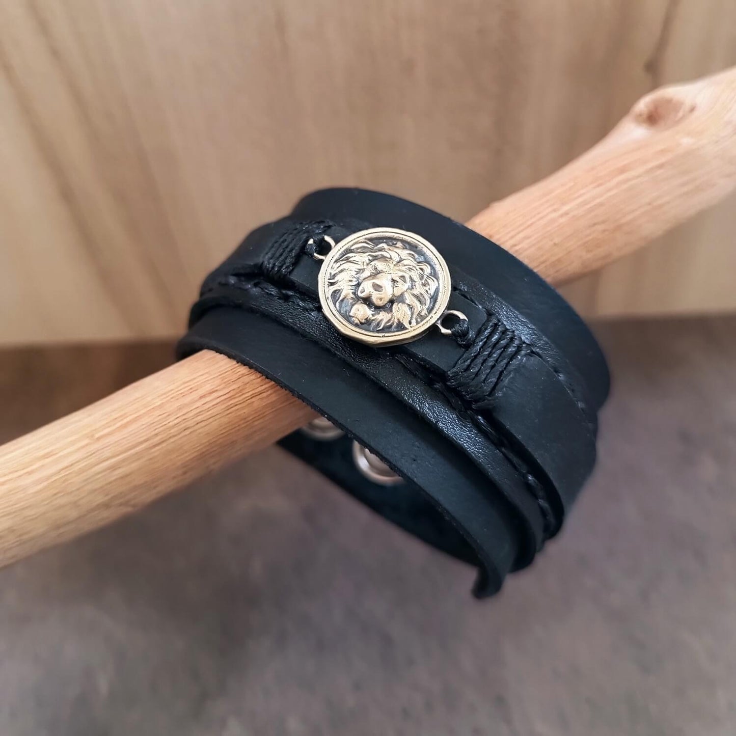 Black leather bracelet with a lion emblem on a wooden stick.
