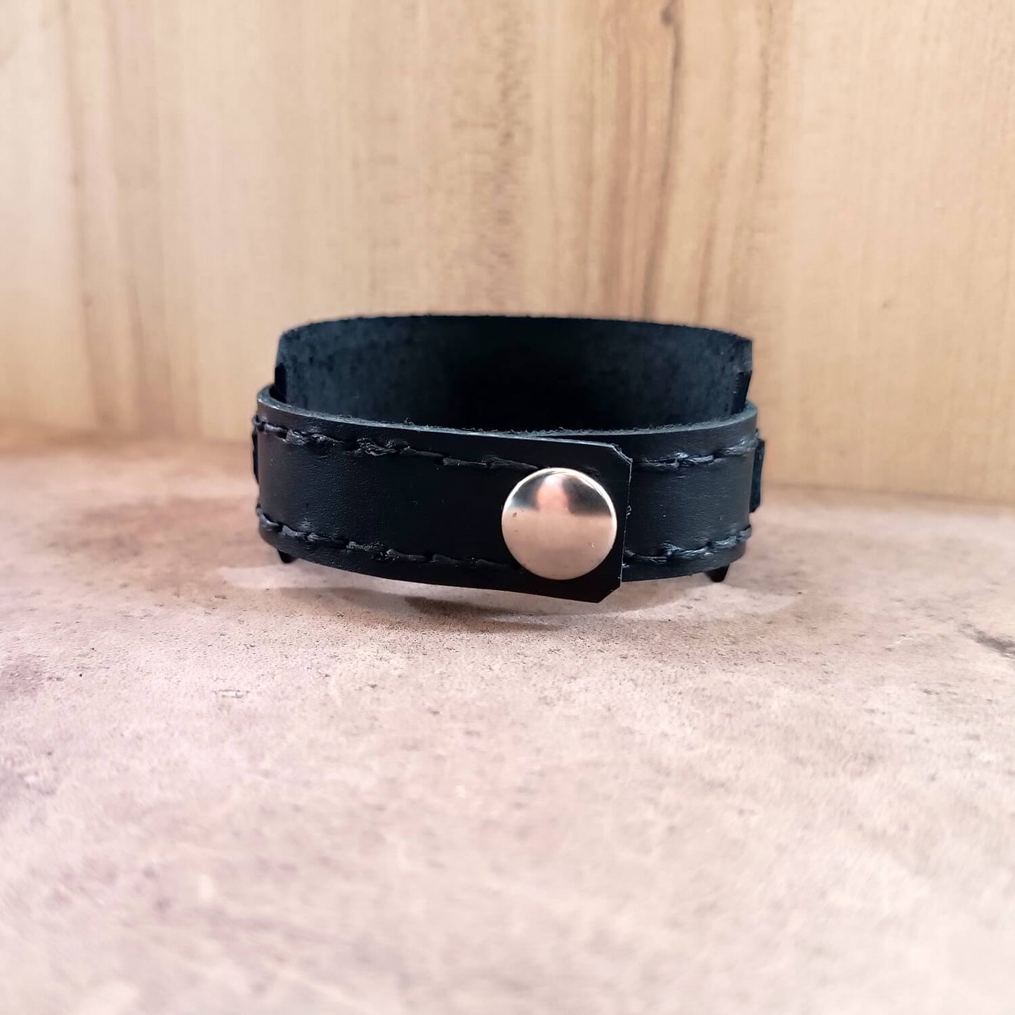 Black leather bracelet with a silver button clasp on a neutral background