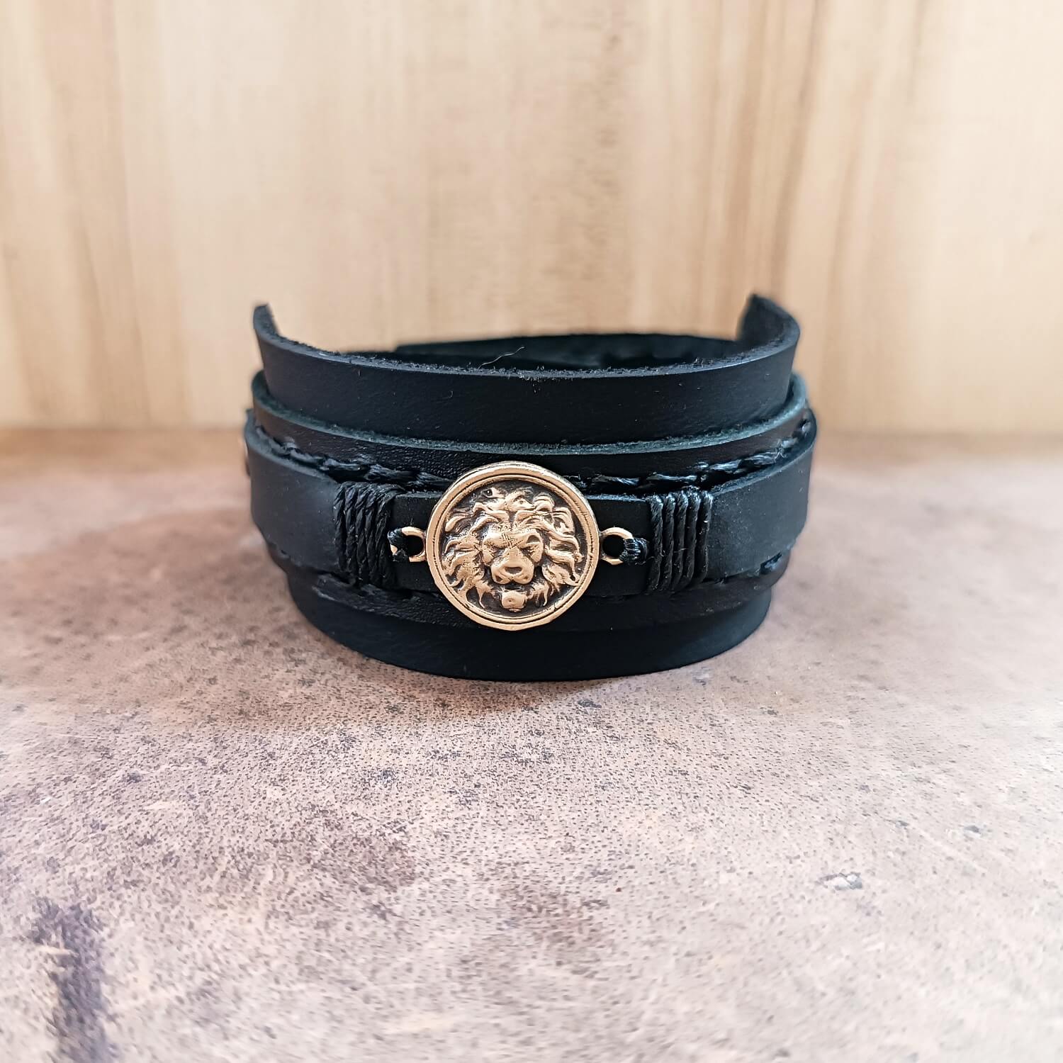 Black leather bracelet with a lion emblem on a textured surface