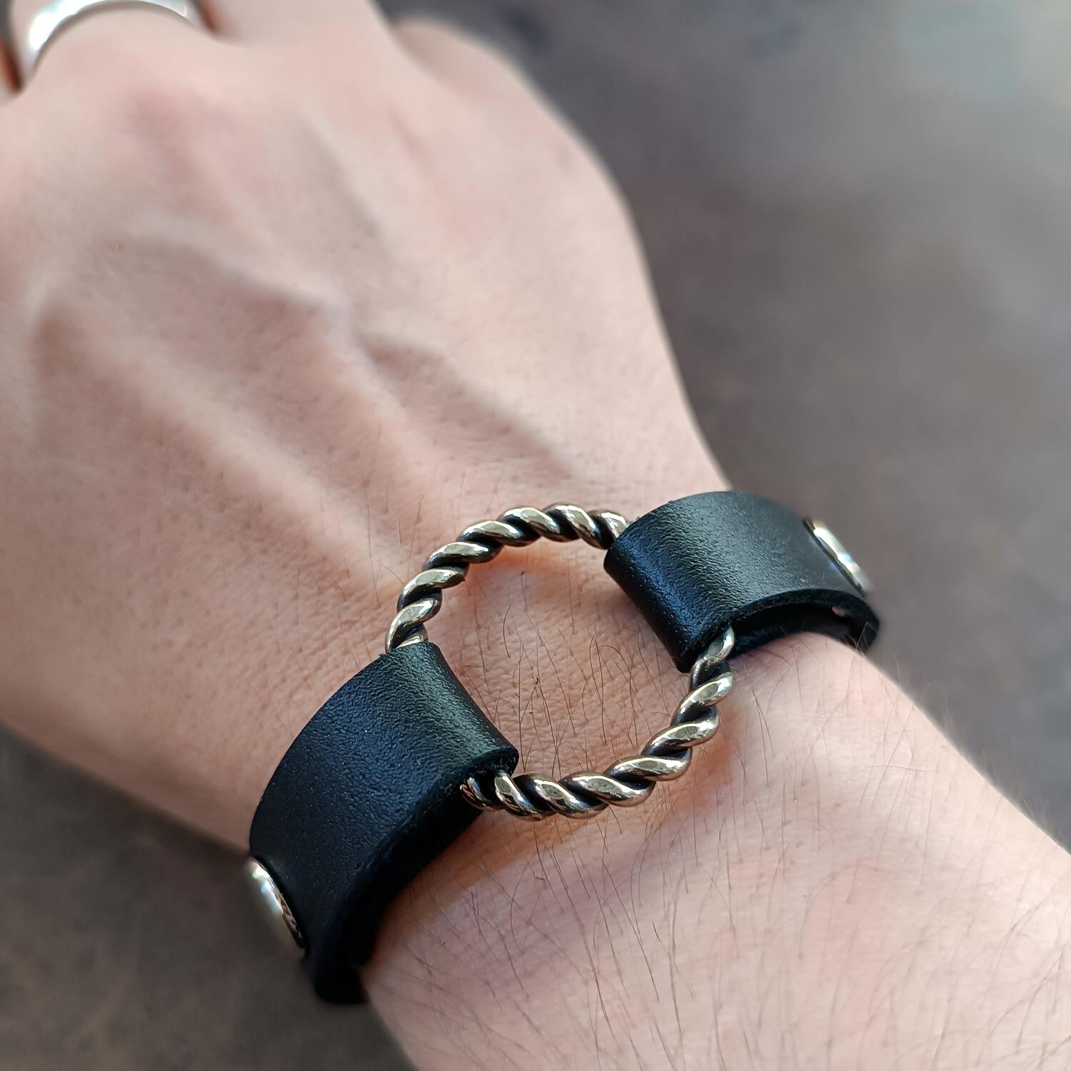 Black leather bracelet with a silver ring on a wrist against a neutral background