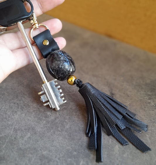 the black tassel keychain clipped on a key, held in hand