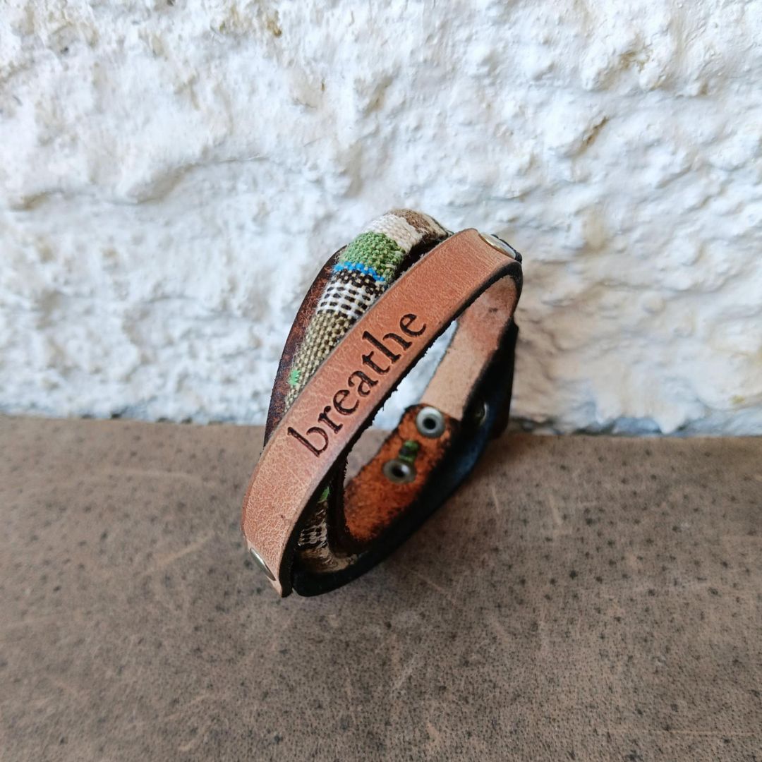 A handmade leather cuff bracelet with a distressed green and brown finish,  resting on a textured brown surface.
