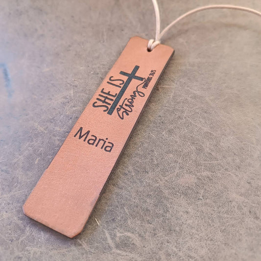 Bookmark with 'SHE IS Strong' text and cross design on a textured surface