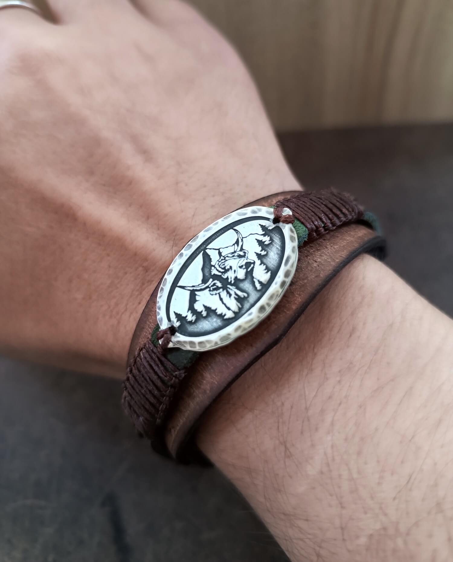 Detailed close-up of the hand-finished Sterling Silver Buffalo Head pendant (oxidized) set against the layered Crazy Horse leather background. Focus on hammered frame, worn on wrist.
