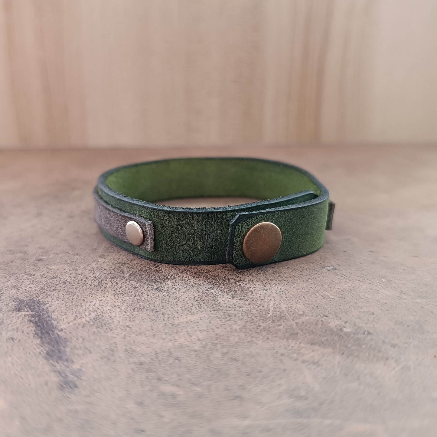 Green leather bracelet with metal clasps on a textured surface back view