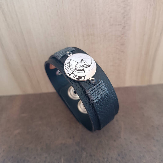 Black leather bracelet with a silver St. Charbel pendant on a wooden surface