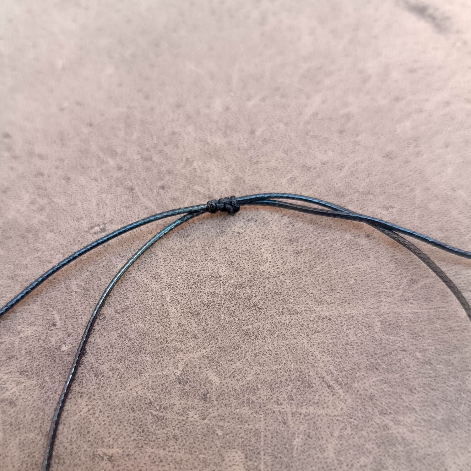 Close-up of a thin black cord or string tied in a knot, laid on a textured gray surface.