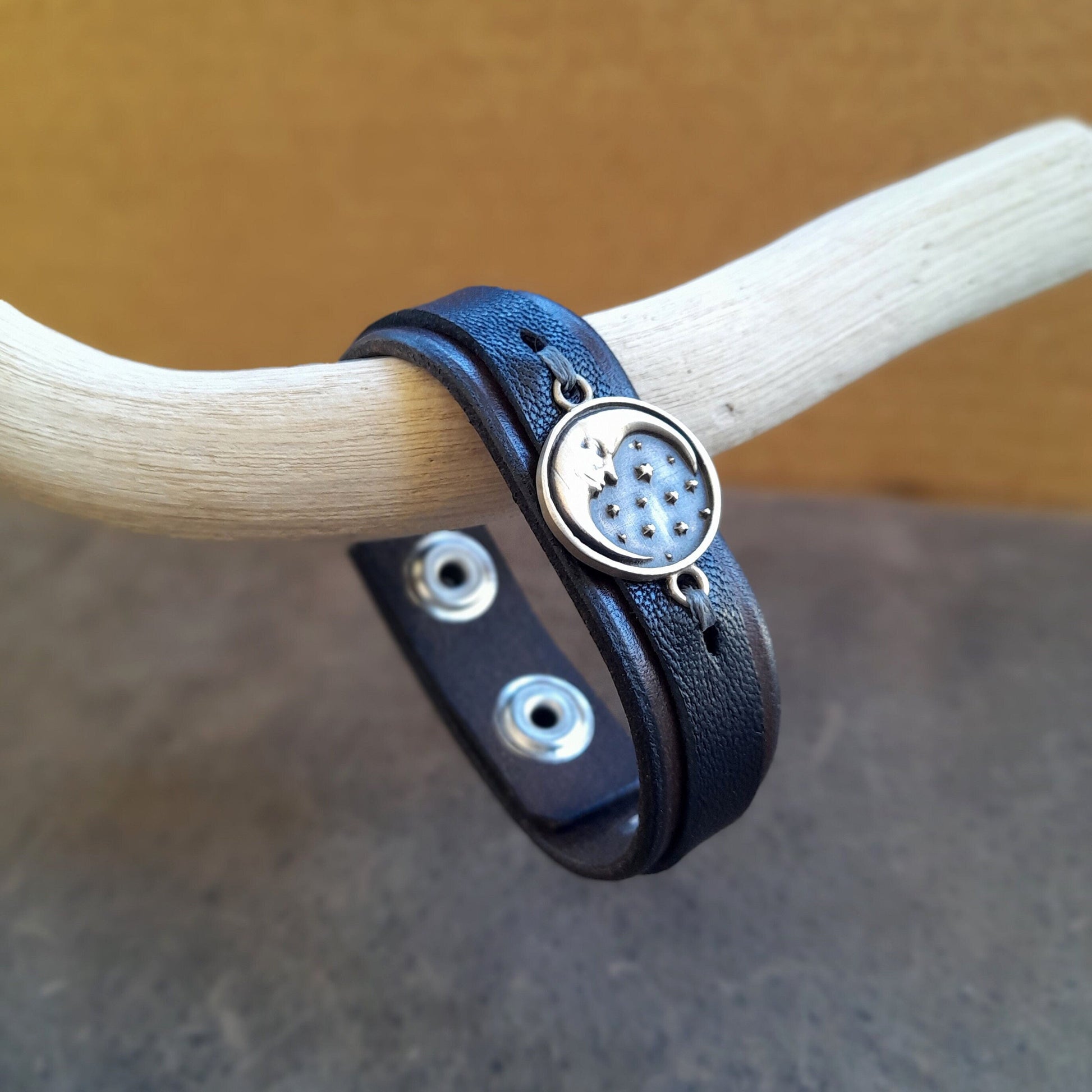 close up side view of the crescent moon pendant on the layered leather bracelet