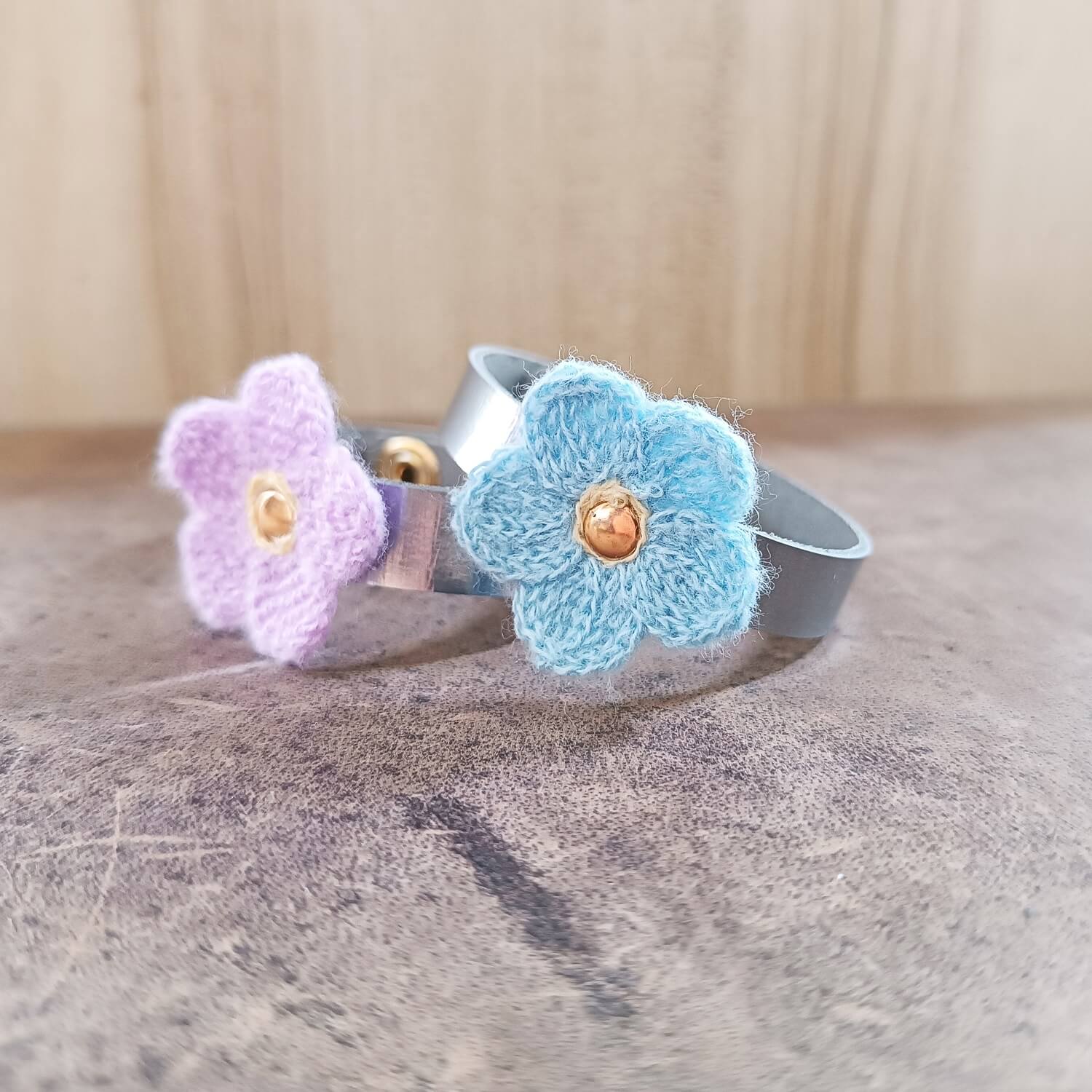 Two silver leather bracelets with crocheted flowers on a textured surface