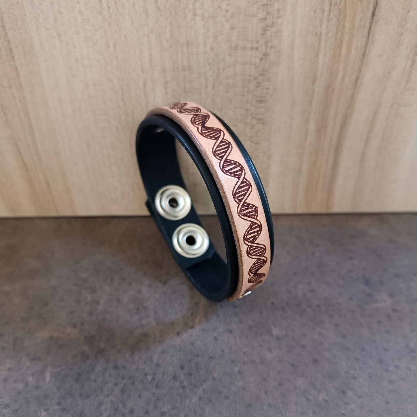 Black and light brown leather bracelet with DNA pattern on a wooden surface