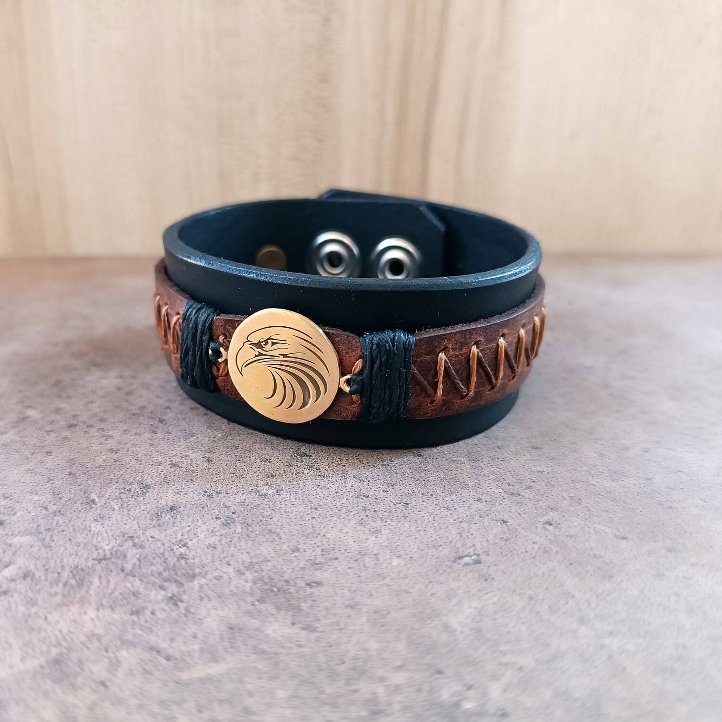 Front  full view of men's wide black leather cuff bracelet with laser engraved tribal eagle head pendant and brown zigzag hand-stitching.