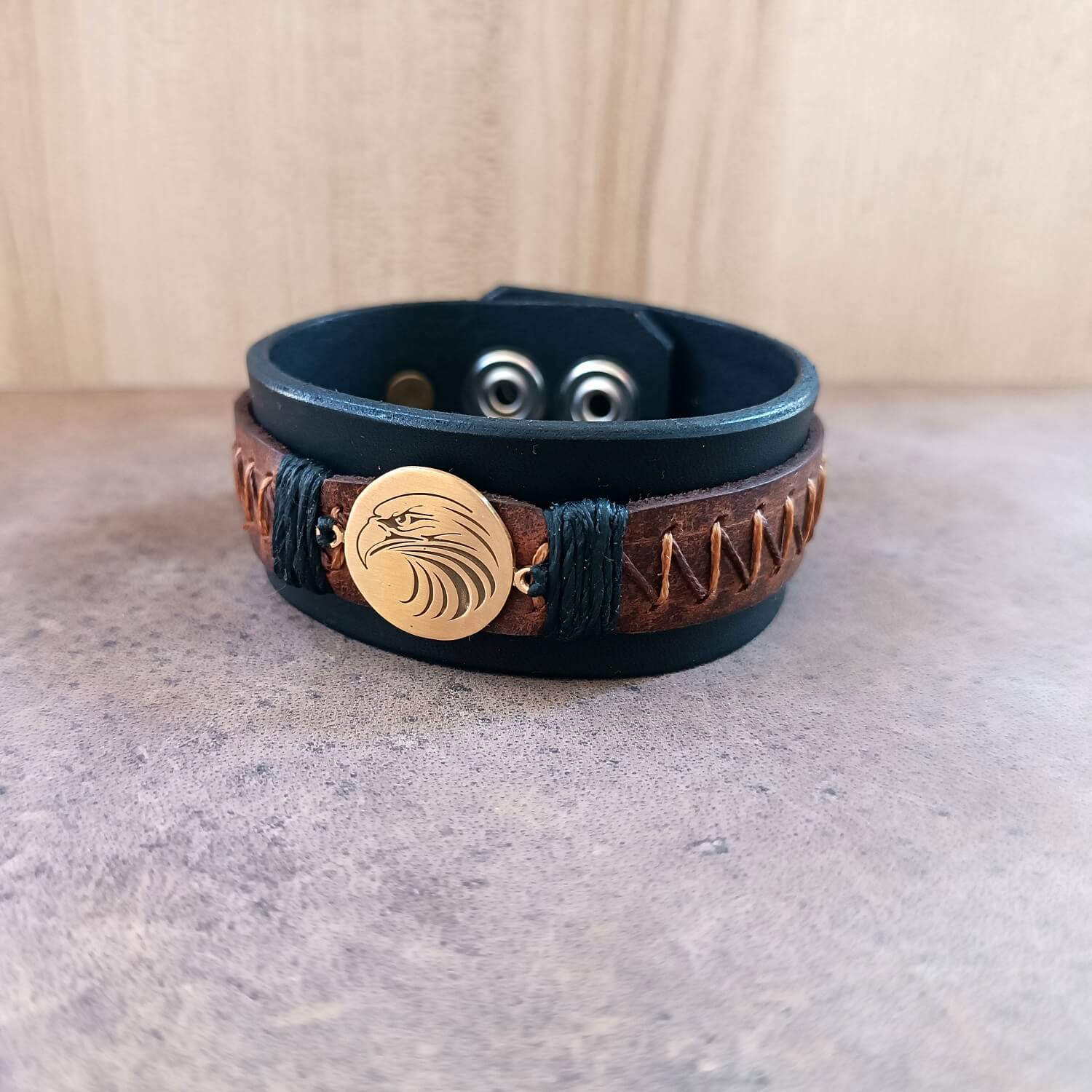 Front  full view of men's wide black leather cuff bracelet with laser engraved tribal eagle head pendant and brown zigzag hand-stitching.