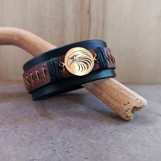 Front view of men's wide black leather cuff bracelet with polished brass tribal eagle head pendant and brown zigzag hand-stitching.