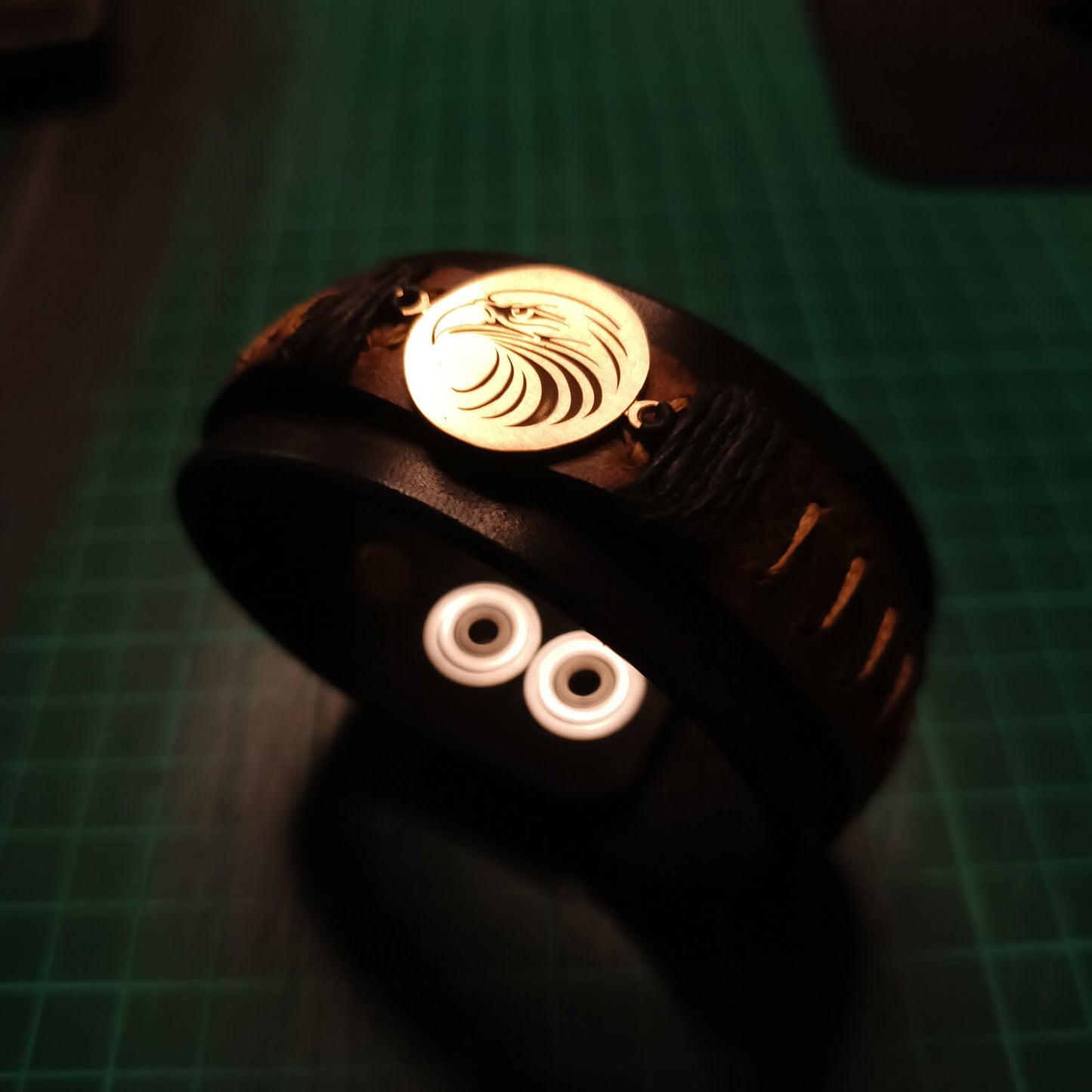 Close-up of laser-engraved tribal eagle head on brass pendant for leather cuff.