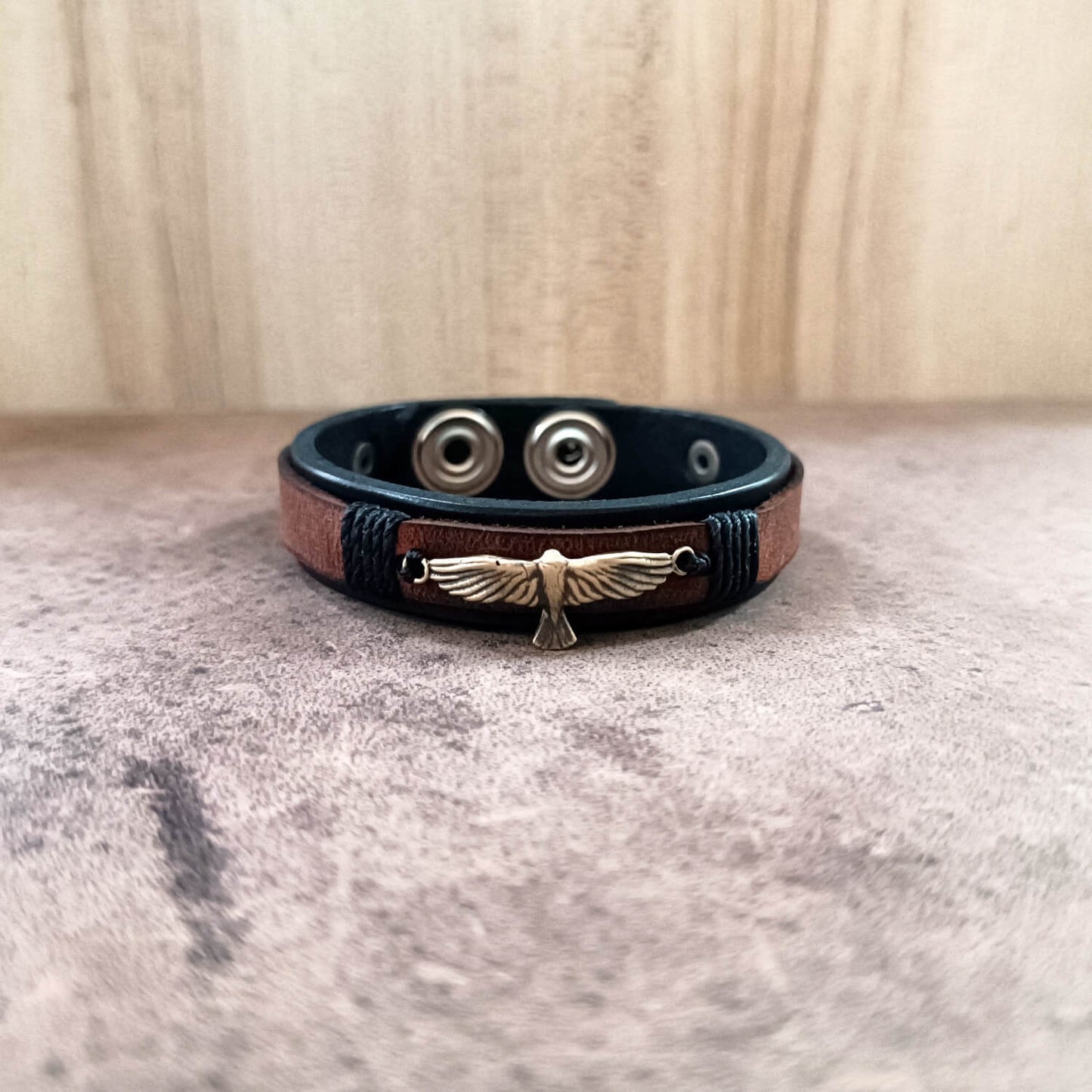 Leather bracelet with metal eagle charm on a textured surface