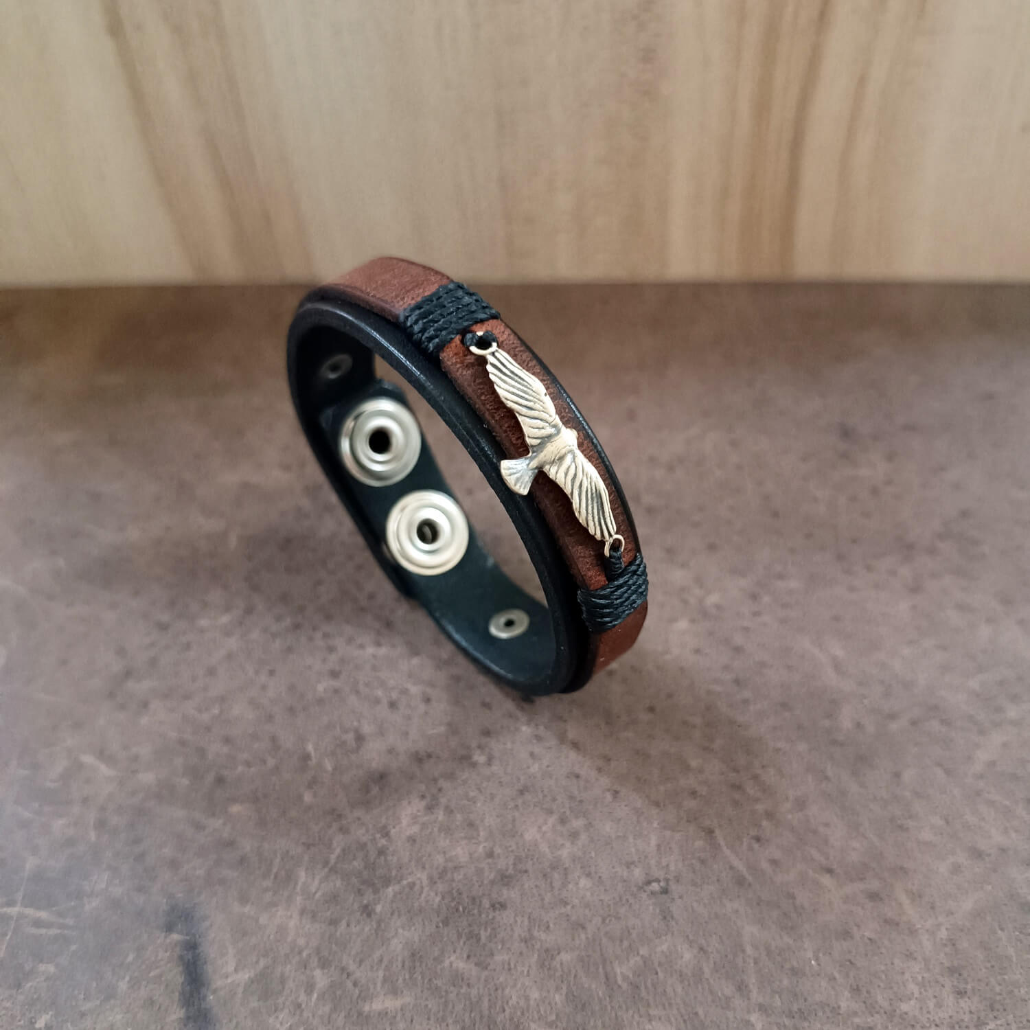 Bracelet with leather strap and metal eagle on a wooden surface