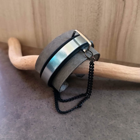 Industrial Gray and Black Edgy Leather Cuff with a chain on a wooden stick against a wooden background