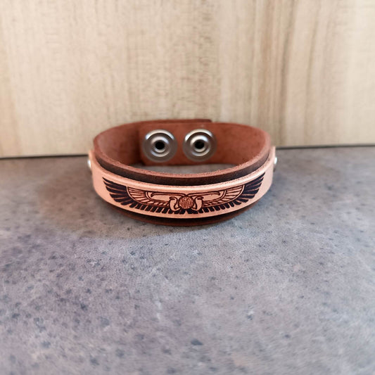 Brown leather bracelet with winged disc Symbol on a gray surface