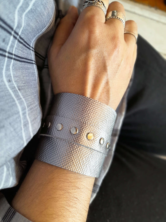 Hand wearing a silver cuff with decorative elements on a blurred background