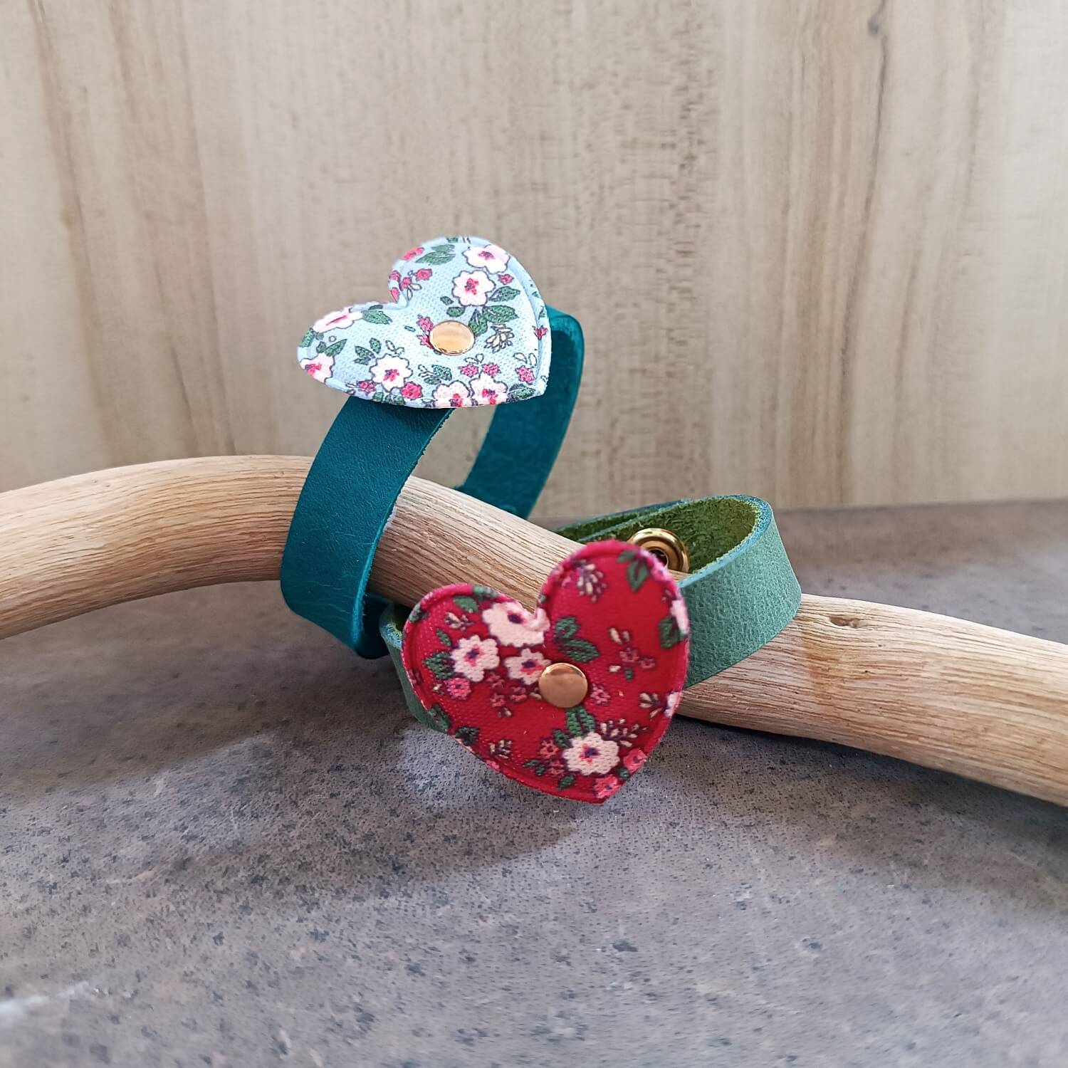 Two handmade leather bracelets for girls, one green with red floral fabric heart and one petrol blue with light blue floral heart angle view