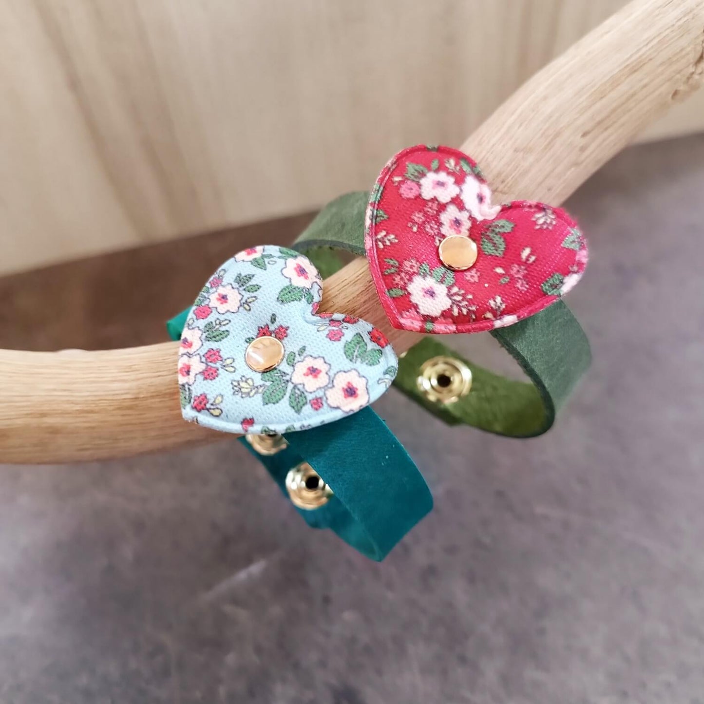 Two handmade leather bracelets for girls, one green with red floral fabric heart and one petrol blue with light blue floral heart close up