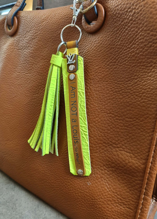Yellow tassel keychain with 'I am not a Louis' text on a brown leather bag.