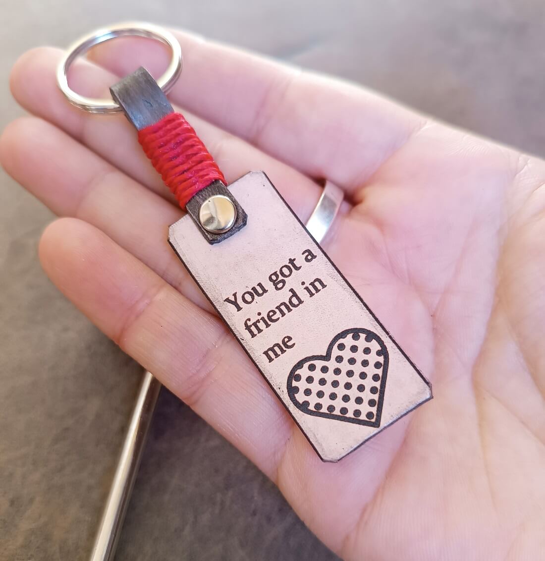 Keychain with 'You got a friend in me' text and heart design held in a hand.