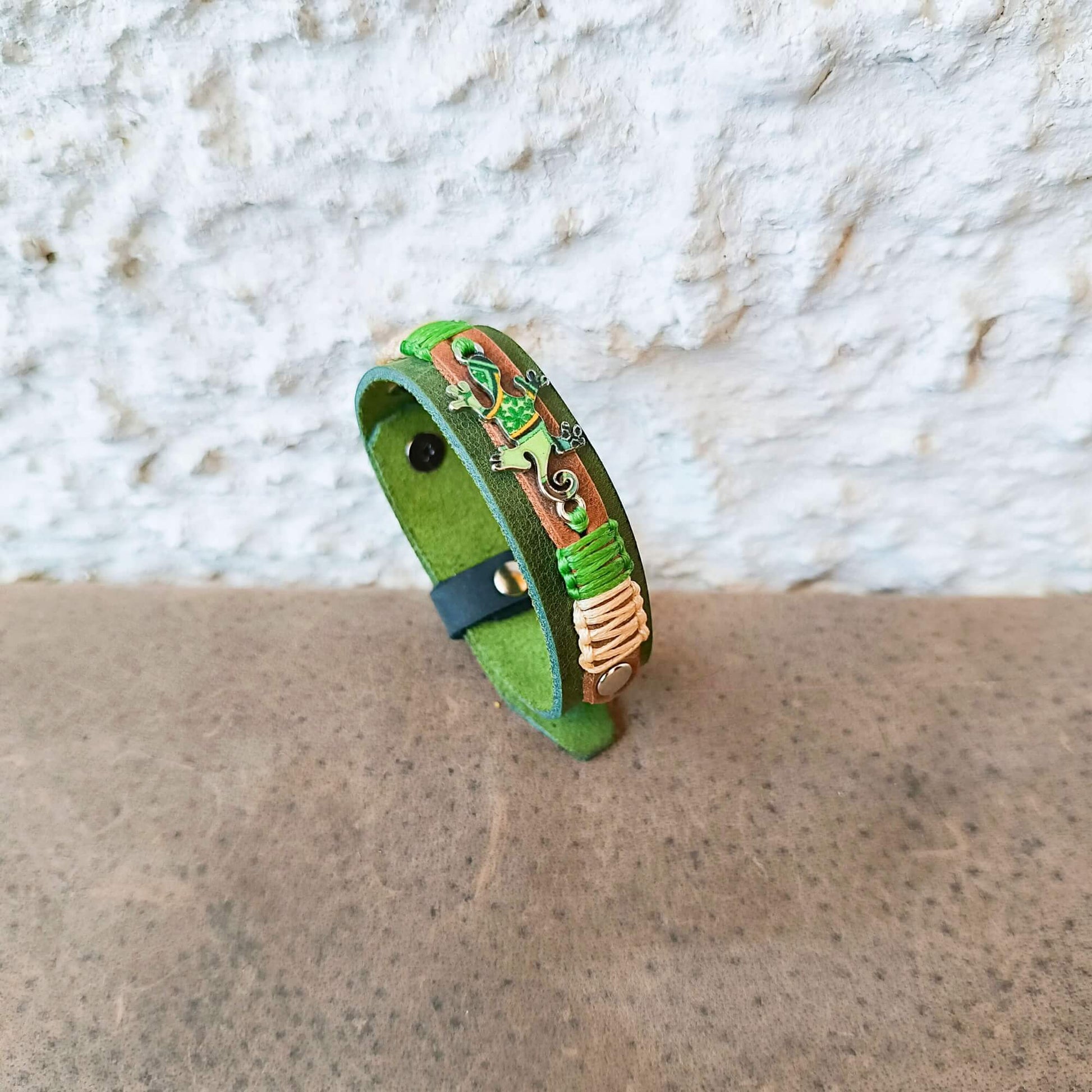 A handmade green leather cuff bracelet with colorful gecko motif and macrame cords.
