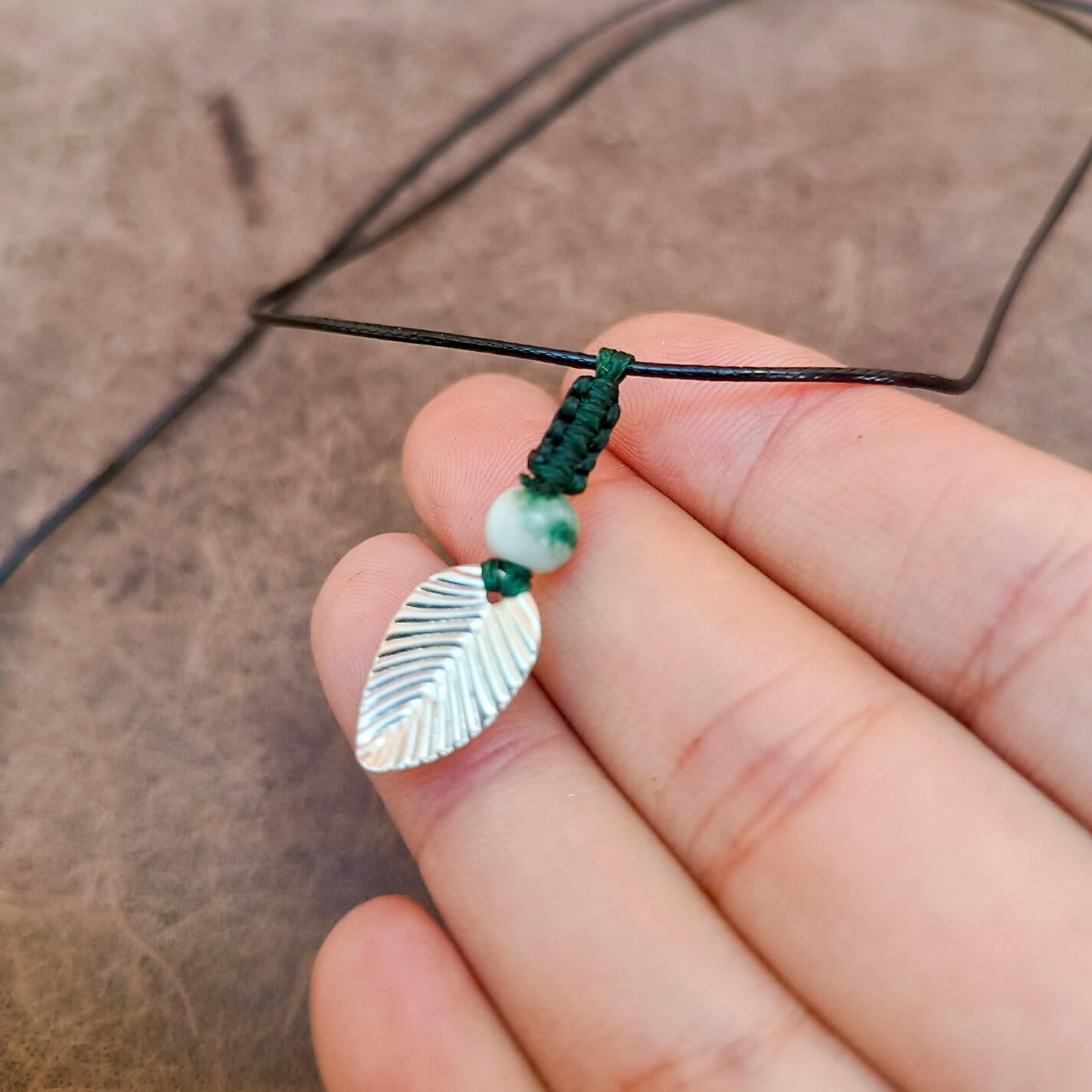 silver leaf pendant necklace with green jasper and forest green macrame spine held on hand
